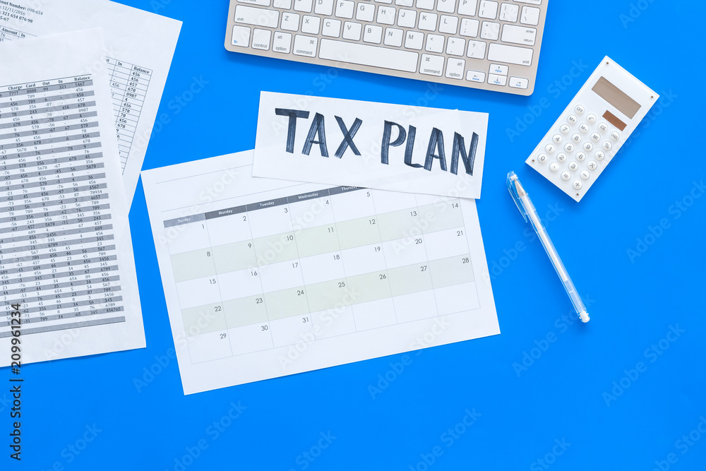 Tax plan words on office work desk with bills, keyboard, coffee, glasses on blue background top view copy space Tax plan words on office work desk with bills, keyboard, coffee, glasses on blue background top view copy space
