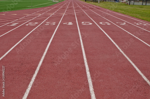 Running lanes on a red track with white numbers and lines with green grass on both sides © woodsnorth