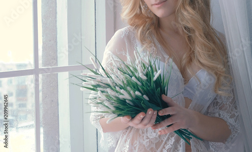 Young slim sexy blond girl in lingerie and boudoir sitting on windowsill and lookingin at artificial flowers in her hands. Closeup body. photo