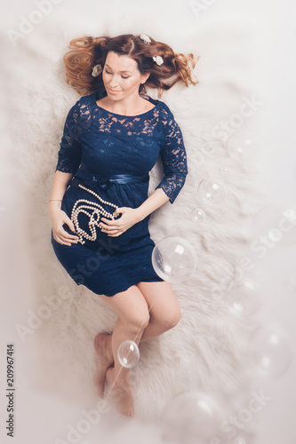 a pregnant woman in a blue dress lying on the floor and holding a of pearls on a background of stomach photo