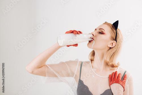 Young girl drinking milk from glass bottle like cat woman. photo