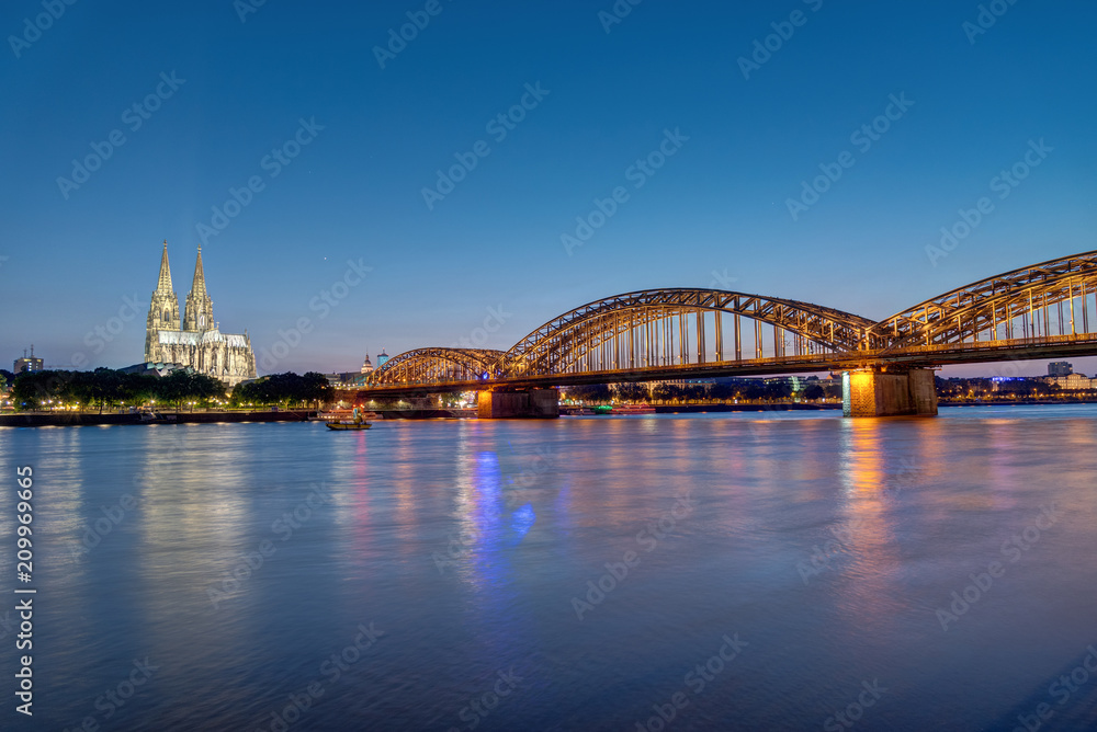 The river Rhine, the Cologne Cathedral and the Hohenzolllern bridge in Cologne at dusk