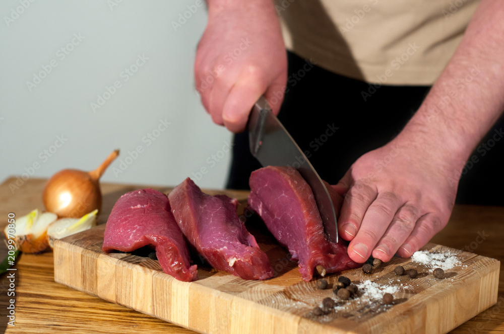 Man cooking beef meat. Male chef preparing pork for cooking. Raw ingredients onion meat salt pepper for cooking beef meat on a wooden table