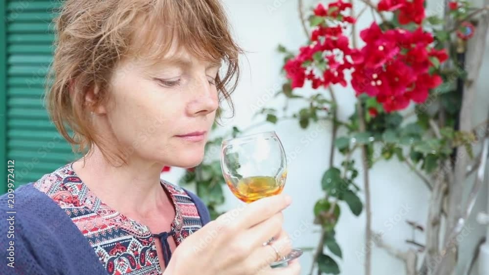 Pretty young woman spending time outdoors, drinking wine on a background of beautiful flowers and enjoying sunny weather Pretty young woman spending time outdoors, drinking wine on a background of beautiful flowers and enjoying sunny weather