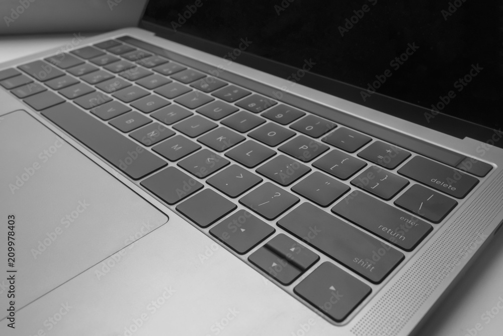 Close up side photo of modern gray laptop with black keyboard, perforation for speaker