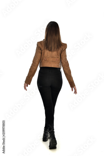 full length portrait of brunette girl wearing brown leather jacket. standing pose with back to the camera on white background.