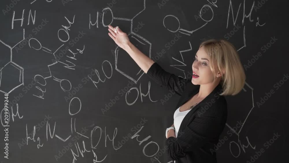 Teacher writing formulas on the chalk Board and explains the students the formula. Teacher writing formulas on the chalk Board and explains the students the formula.