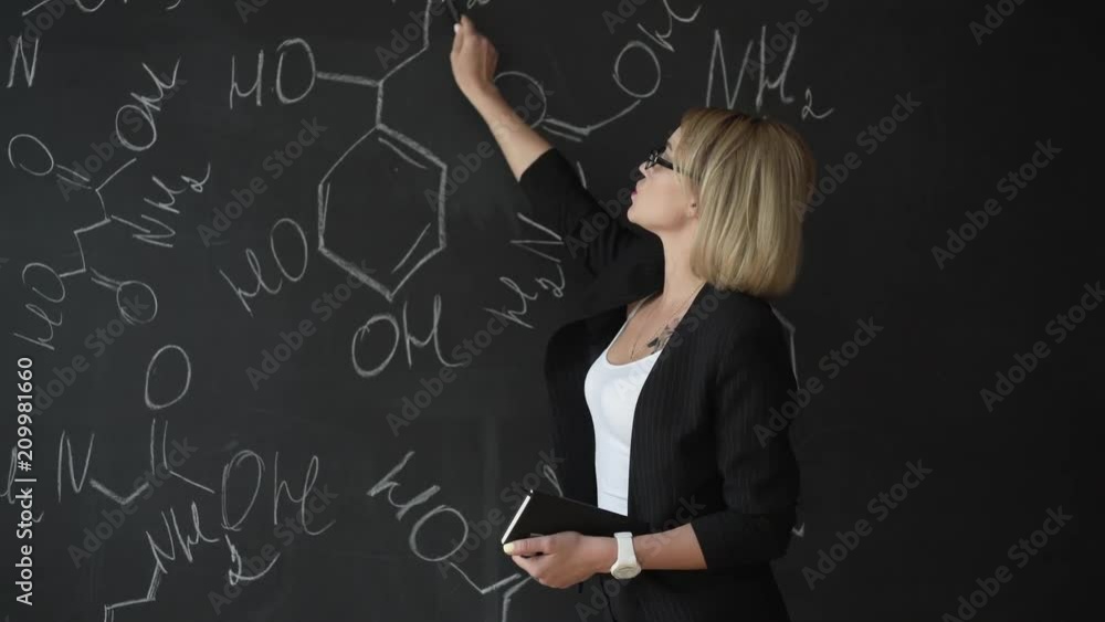 Teacher writing formulas on the chalk Board and explains the students the formula. Teacher writing formulas on the chalk Board and explains the students the formula.