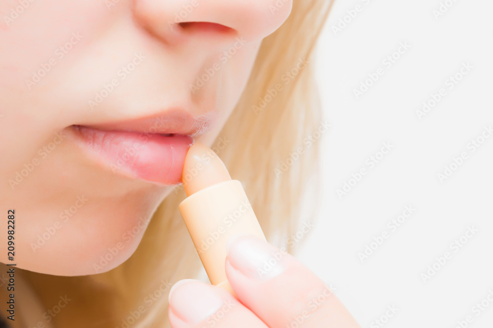 Young woman using natural lips balm. Care about healthy, moisture and soft lips. Protection from cold winter, hot summer and windy time. Empty place for text or logo on light gray background.