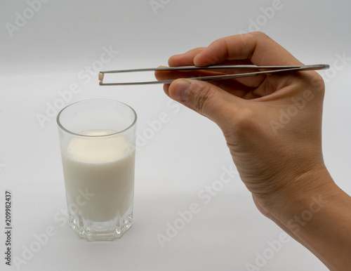 Handing holding milk teeth and little root with tweezer over a glass of milk