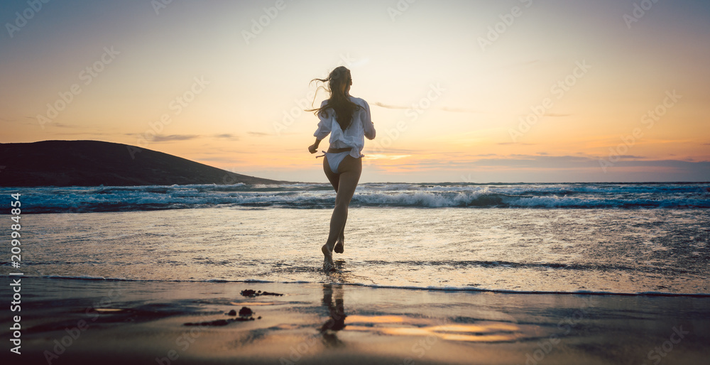 Woman at the beach in sunset running into the water