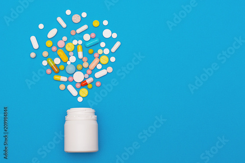 Assorted medical pills and capsules scattered from a bottle on a blue background. Empty place for text. Background. photo