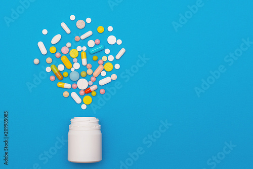 Assorted medical pills and capsules scattered from a bottle on a blue background. Empty place for text. Background.