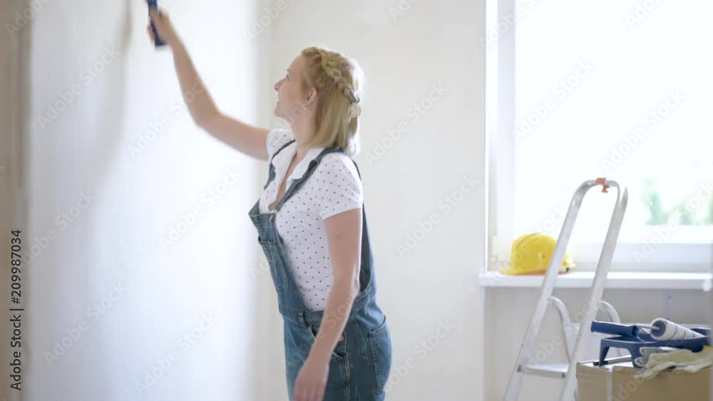 Young family makes repairs in new flat. Beautiful couple - painting wall in apartment. Man and woman doing overhaul of house. Guy and girl making decorate room, laughing and having fun. Young family makes repairs in new flat. Beautiful couple - painting wall in apartment. Man and woman doing overhaul of house. Guy and girl making decorate room, laughing and having fun.