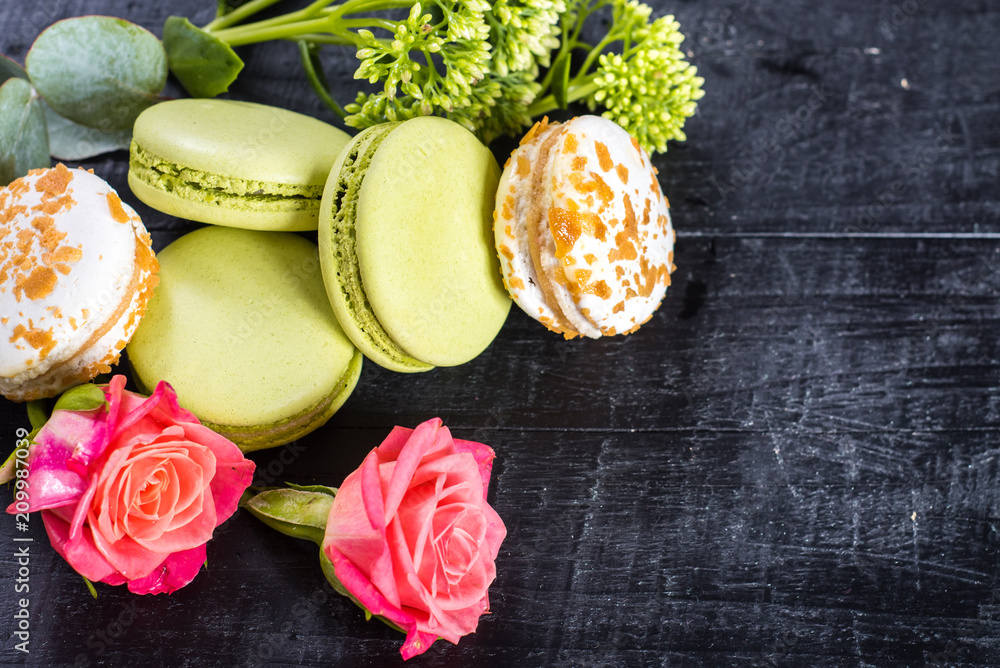 Sweet colored macaroons in composition with flowers on black background. Copy space