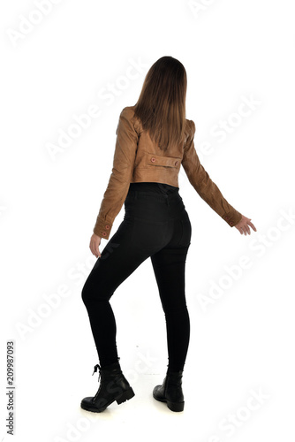 full length portrait of brunette girl wearing brown leather jacket. standing pose with back to the camera on white background.