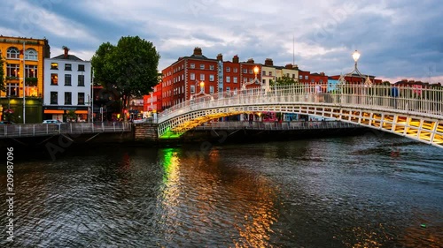Dublin, Ireland. Night view of famous illuminated Ha Penny Bridge in Dublin, Ireland. Time-lapse at sunset. Light to dark, zoom in
