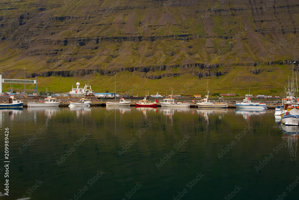 Boats docked in sea on mountain landscape in Sejdisfjordur, Iceland. Water crafts at sea coast. Travelling by water. Adventure and discovery. Summer vacation and wanderlust