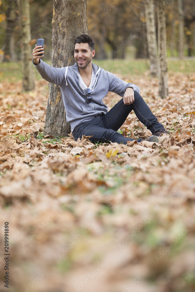 Handsome man in nature taking selfie pictures with his smartphone. Autumn. Copy space Handsome man in nature taking selfie pictures with his smartphone. Autumn. Copy space
