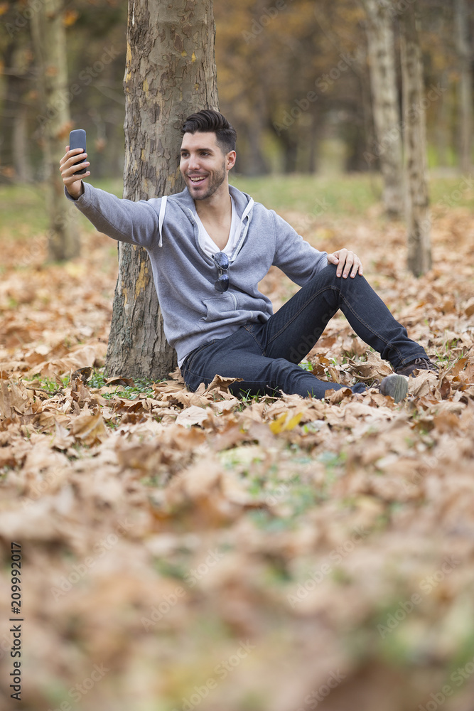 Handsome man in nature taking selfie pictures with his smartphone. Autumn. Copy space
