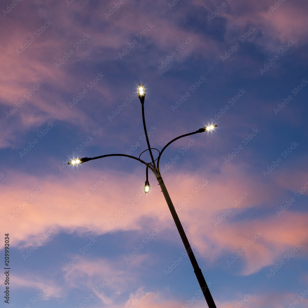 modern street lamp shines against a background of red clouds and a blue sky at sunset, twilight