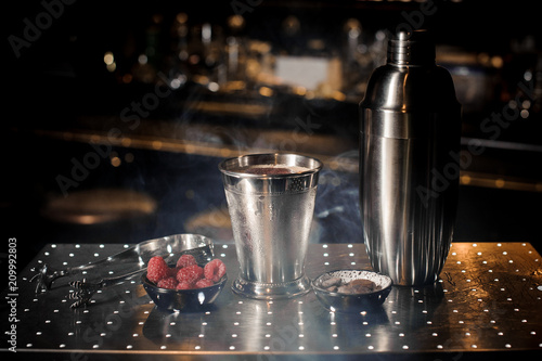 Steel shaker, tweezzers, cup and saucer with raspberry in the smoke photo