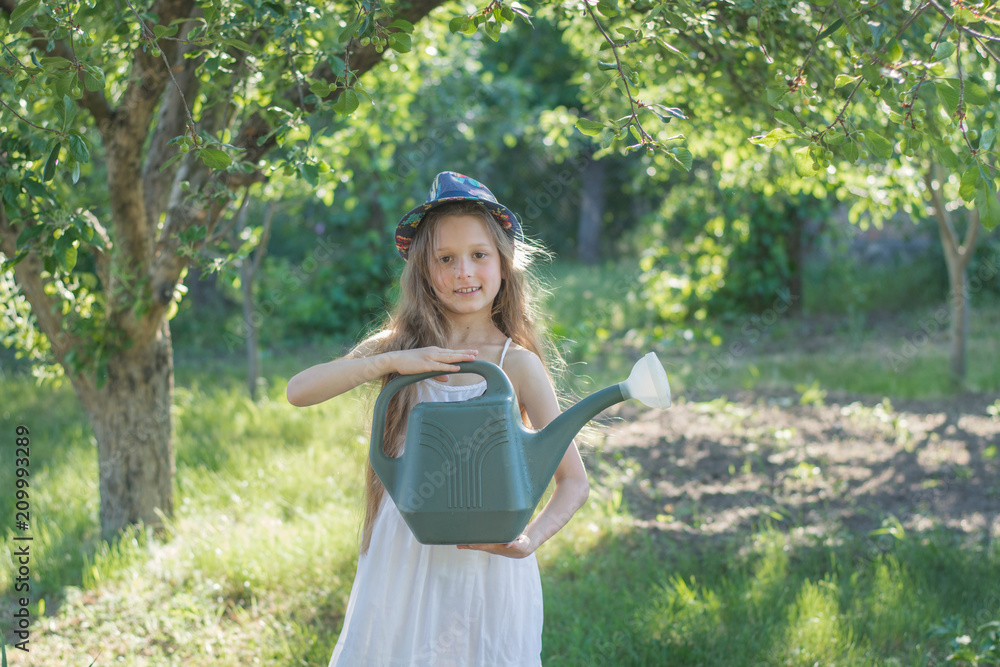 Girl in the garden with a watering can. Girl watering the garden. A child in a white dress in nature Girl in the garden with a watering can. Girl watering the garden. A child in a white dress in nature