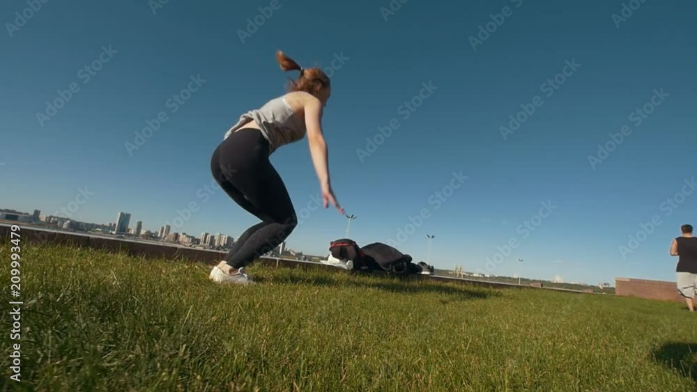 Young female gymnast performs jumps on the grass in sunny day Young female gymnast performs jumps on the grass in sunny day