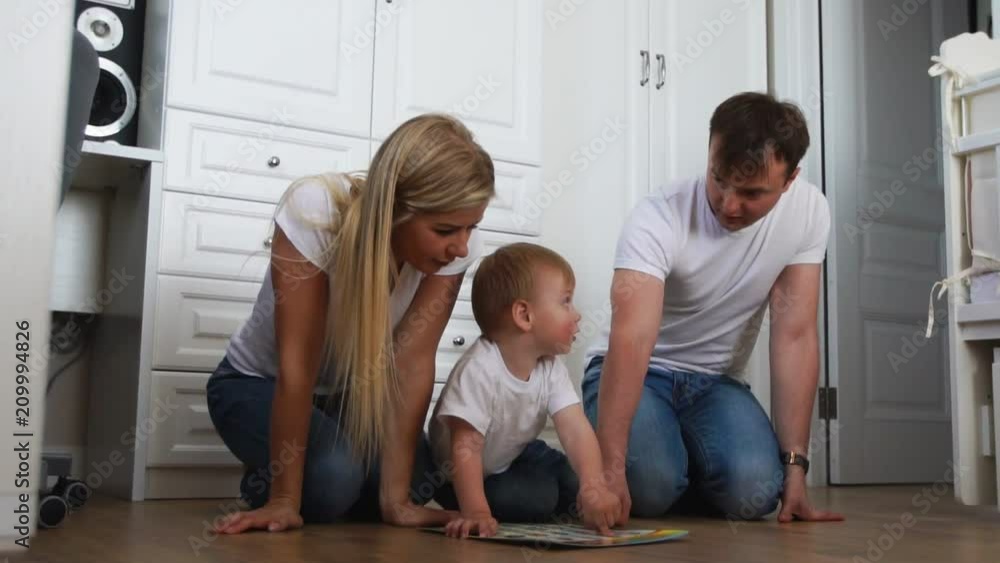 A family of three in white T-shirts and blue jeans sitting on the floor of their bedroom playing with the boy in intellectual games. Slow-motion shooting happy family A family of three in white T-shirts and blue jeans sitting on the floor of their bedroom playing with the boy in intellectual games. Slow-motion shooting happy family