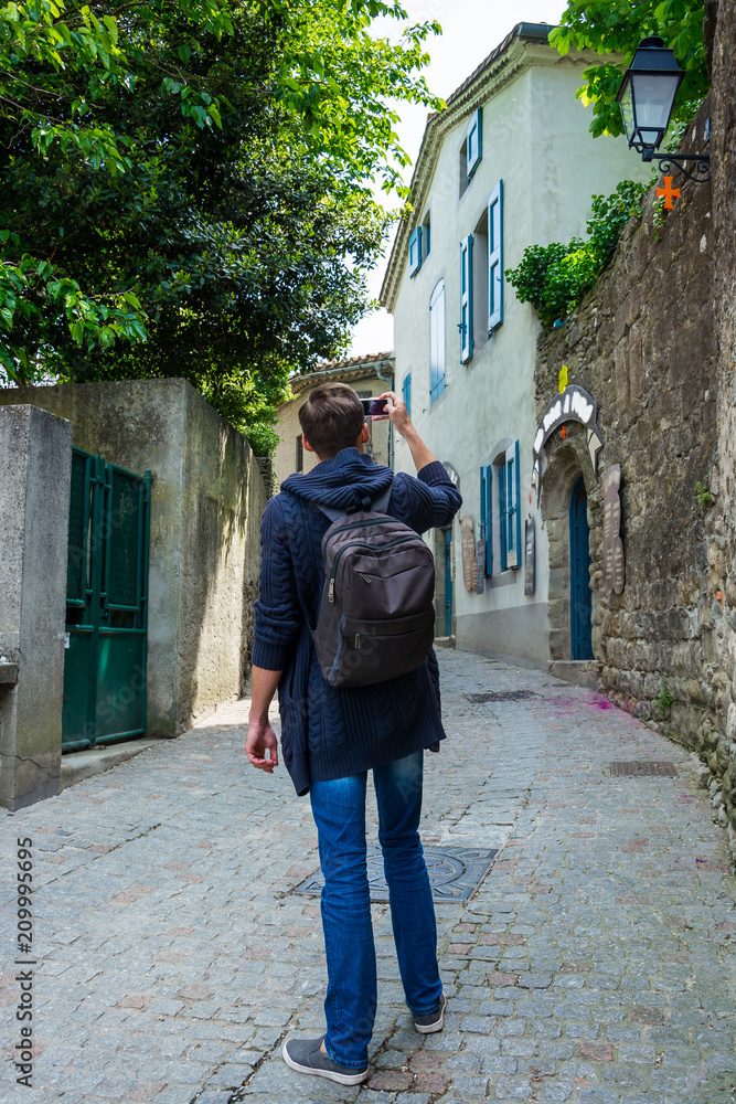 A young man with backpack shoots with a smartphone on the street of the medieval city Carcassonne in France