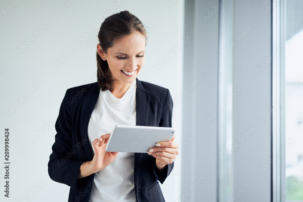 Cheerful businesswoman using digital tablet standing at office Cheerful businesswoman using digital tablet standing at office