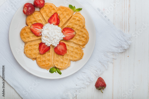  Norwegian heart shaped waffles topped with strawberries,  mint and whipped cream on white plate and white wooden background. St. Valentine's Day breakfast. Romantic breakfast. Copy space