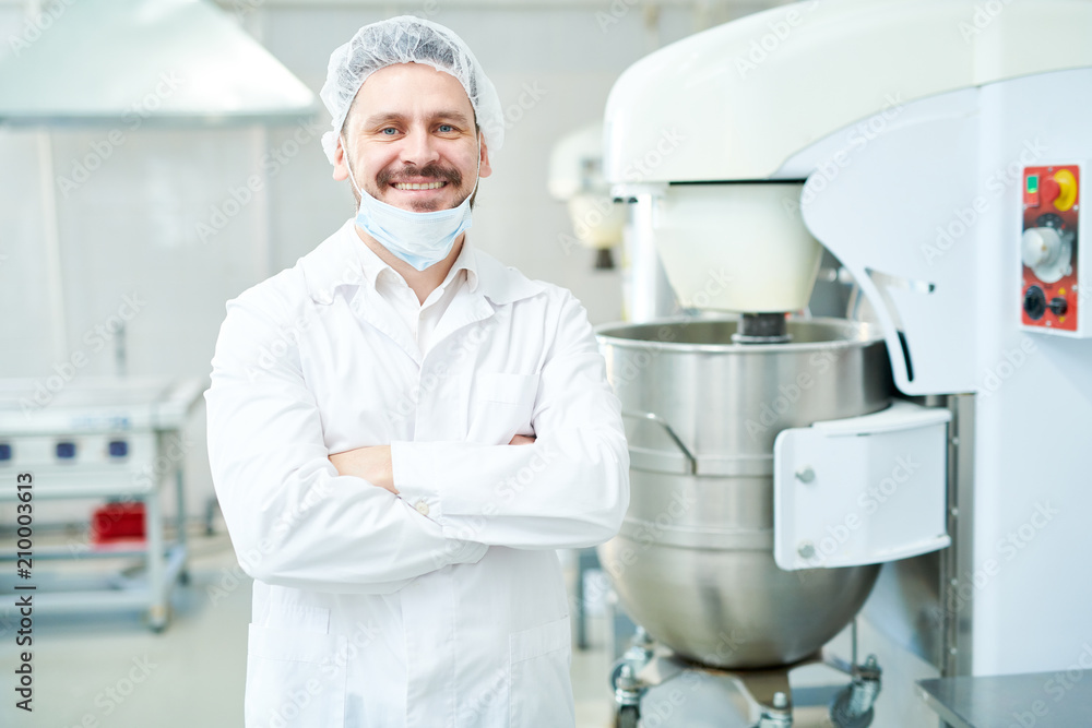 Happy confectionery factory employee standing in white coat with arms crossed and looking at camera. 