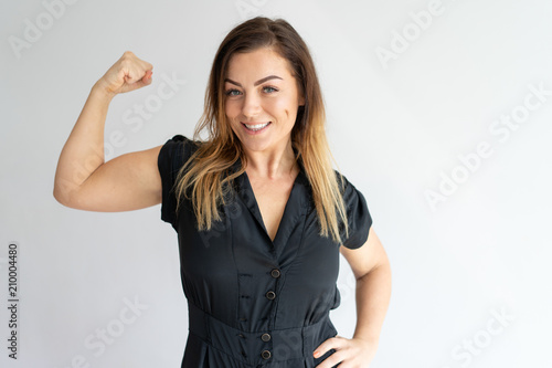 Positive joyful lady showing hand muscles. Middle aged Caucasian woman in casual wear flexing bicep. Strength or feminism concept