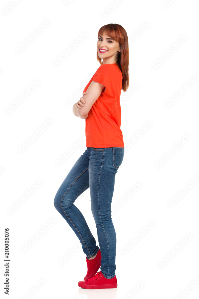 Smiling Young Woman Is Standing Relaxed With Arms Crossed And Looking At Camera. Side View. Smiling Young Woman Is Standing Relaxed With Arms Crossed And Looking At Camera. Side View.