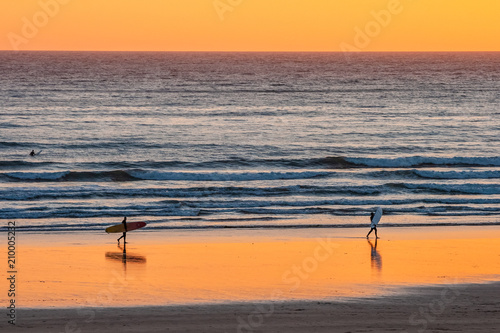 Distant surfers silhouettes on the beach at sunset, Devon, England