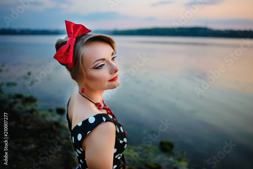 A beautiful young woman dressed standing by the lake, on the background of the sunset