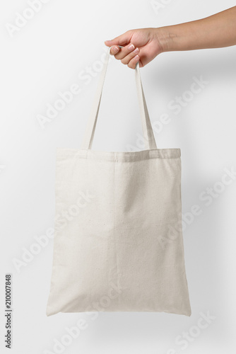 Mockup of female hand holding a blank Tote Canvas Bag on light grey background. High resolution. 