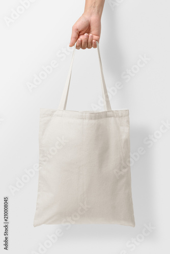 Mockup of female hand holding a blank Tote Canvas Bag on light grey background. High resolution. 