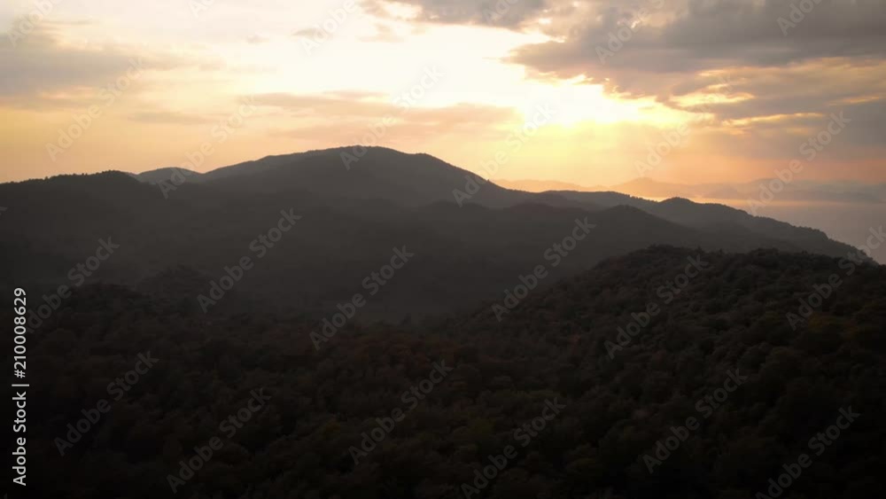 Aerial view circling around a mountain side covered in dense forest at sunset Aerial view circling around a mountain side covered in dense forest at sunset