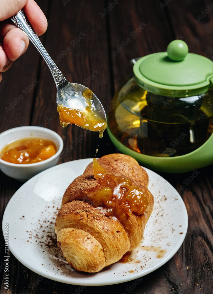 chef pours jam to croissant, fresh croissants with jam on dark wooden table and tea with rosemary, chocolate on food