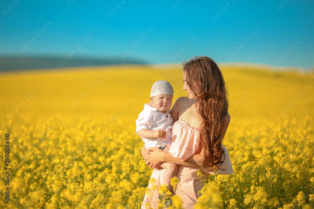Happy family summer vacation. Mother with son in rape field enjoying life at sunset. Pretty brunette with long healthy hair. Carefree girl over yellow field and blue sky. Countryside landscape. Happy family summer vacation. Mother with son in rape field enjoying life at sunset. Pretty brunette with long healthy hair. Carefree girl over yellow field and blue sky. Countryside landscape.