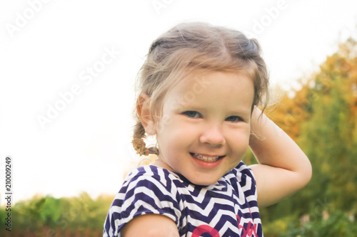 Girl posing on camera. the child holds his hand behind his head, the frame shows her elbow. The little child looks directly at the viewer and smiles