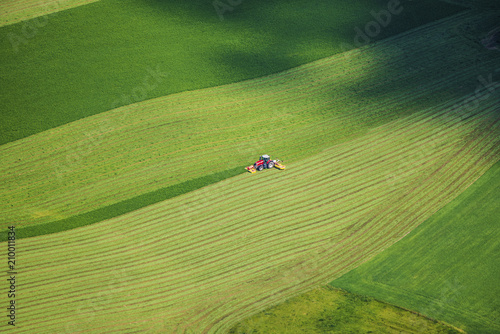 Red tractor working on beautiful green field in summer - bird eye perspective