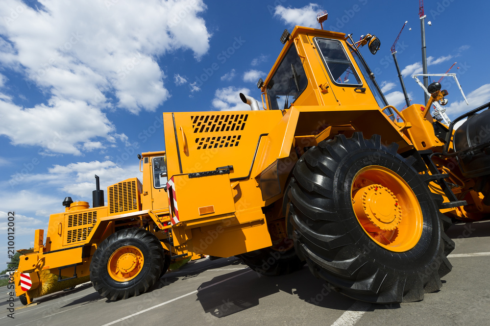 Construction machines, huge orange powerful tractor, front end loader and bulldozer with black wheels in row, heavy industry, bottom view, cranes, white clouds and blue sky on background 