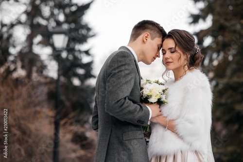 Loving and beautiful bride and groom stand in an embrace in the winter forest