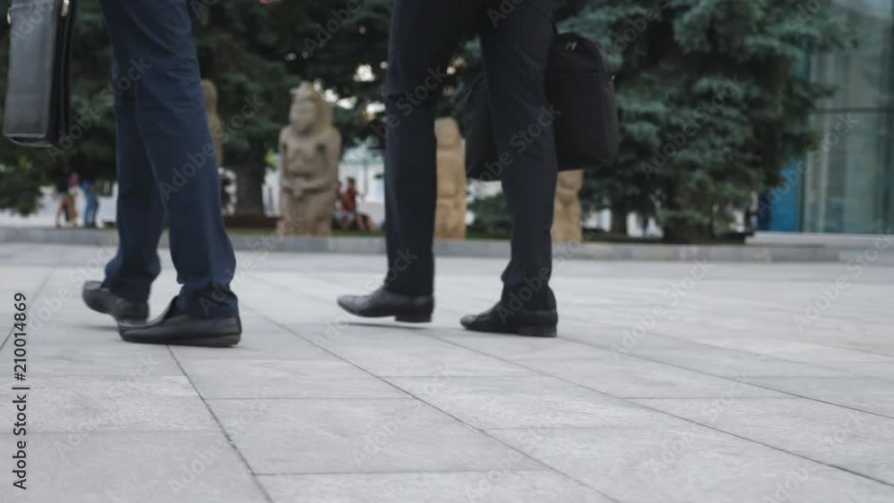 Feet of two businessmen walking in city street. Business men commute to work together. Confident guys being on his way to office. Legs of colleagues going outdoor. Slow motion Close up Feet of two businessmen walking in city street. Business men commute to work together. Confident guys being on his way to office. Legs of colleagues going outdoor. Slow motion Close up