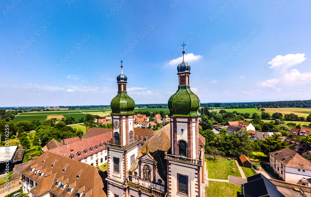 Obraz premium Soaring majestic church Saint Maurice in little french village Ebersmunster. Aerial drone view.