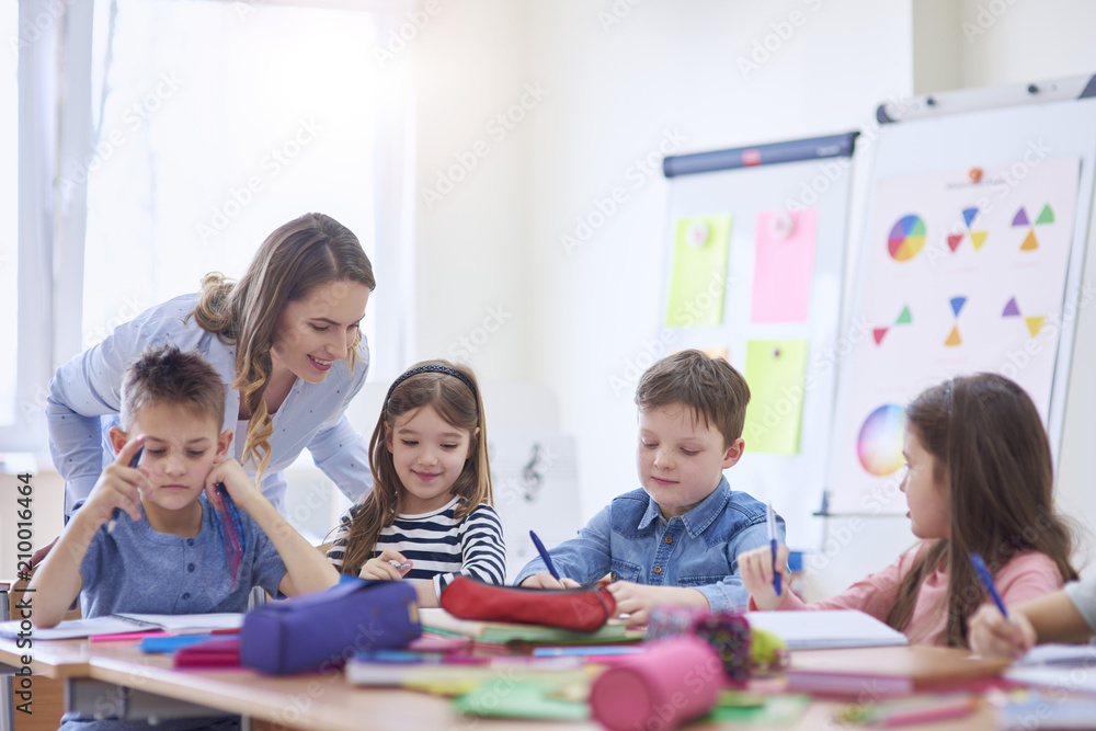 Smiling teacher helping pupils with their tasks in class Smiling teacher helping pupils with their tasks in class