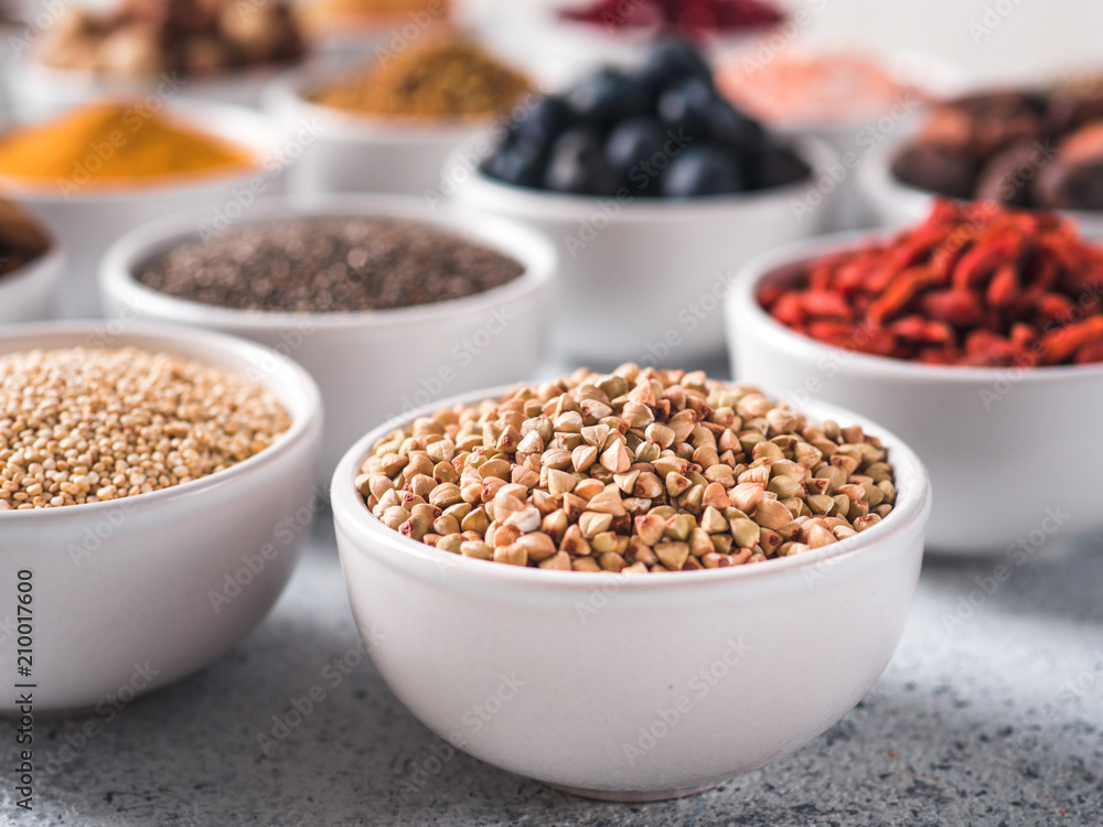 Raw green buckwheat in small white bowl and other superfoods on background. Selective focus. Different superfoods ingredients. Concept and illustration for superfood and detox food Raw green buckwheat in small white bowl and other superfoods on background. Selective focus. Different superfoods ingredients. Concept and illustration for superfood and detox food
